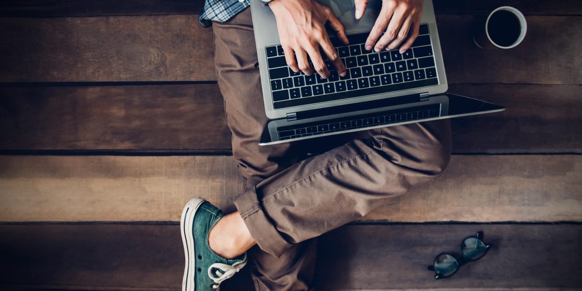 AdobeStock_298839437 businessman sitting on wooden floor with coffee cup and glasses using laptop working at home to send and send reply to email Message customer service